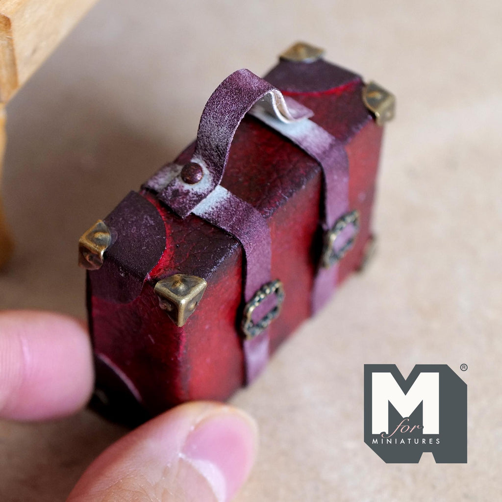 1:12 scale miniature burgundy faux leather suitcase with an aged worn finish, eight antique copper corner caps, two buckle straps and a top handle