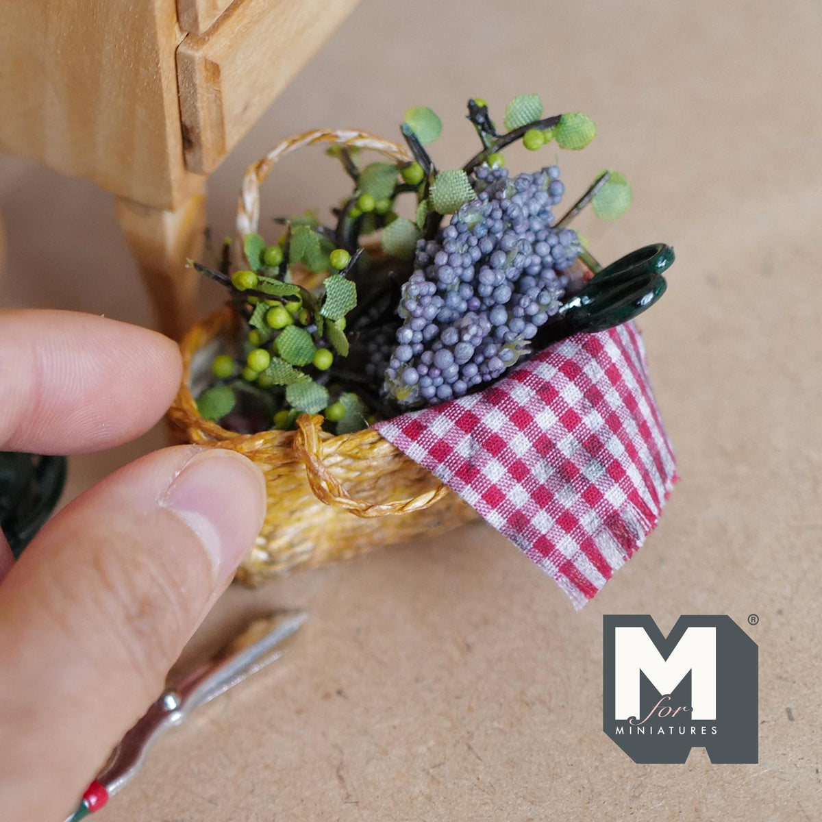 1:12 scale miniature woven harvest basket with a carry handle, purple grapes, leafy sprigs with green berries, a gingham cloth and a pair of scissors
