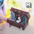 1:12 scale miniature burgundy Christmas storage trunk with brass corners and clasp, lid fixed open, filled with a frosted tree with baubles, wreath with a red bow, bear in a Santa hat and a string of bulb lights