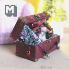 Miniature burgundy Christmas trunk with the lid fixed open, frosted tree inside and a string of colored bulbs draped over the front