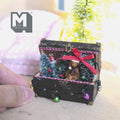 1:12 scale miniature dark brown Christmas storage trunk with corner caps, open lid and checkered lining, filled with a frosted tree, wreath, toy soldier, bear in a Santa hat, checkered blanket and a string of colored bulbs