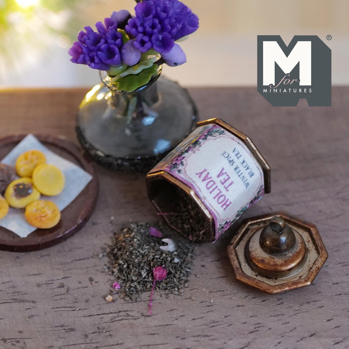 1:12 scale miniature aged metal octagonal tea tin with a pink and purple floral Holiday Tea label, lying on its side with loose tea leaves and pink bits spilling out, its knobbed lid beside it