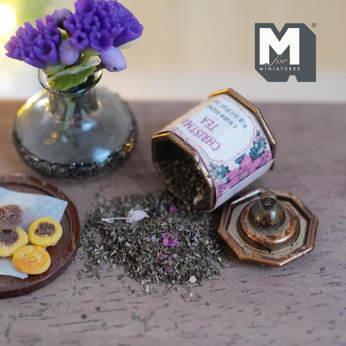 1:12 scale miniature aged metal octagonal tea tin with a pink poinsettia Christmas Tea label, lying on its side with loose tea leaves spilling out, its knobbed lid beside it
