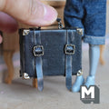 1:12 scale miniature black faux leather suitcase with a worn distressed finish, two buckle straps, metal corner caps and a top handle on metal rings