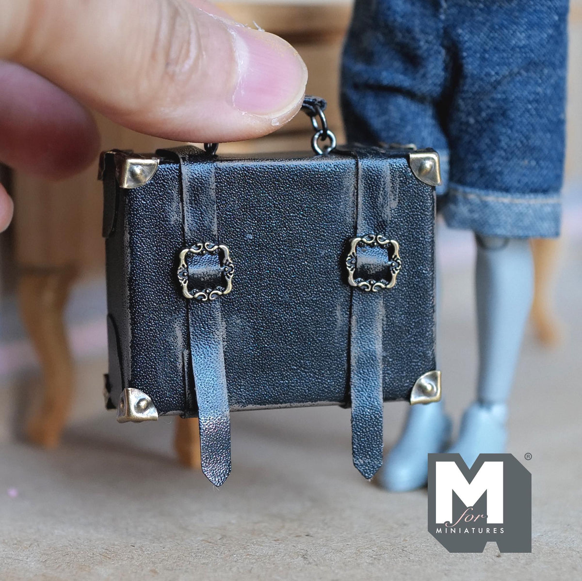 1:12 scale miniature black faux leather suitcase with a worn distressed finish, two buckle straps, metal corner caps and a top handle on metal rings