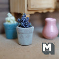 1:12 scale miniature weathered gray clay tapered pot with a raised rim band, planted with a dense cluster of small purple flowers