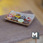 Donuts glacés miniatures sur plaque de cuisson en métal vieilli avec papier sulfurisé à l'échelle 1:12, lot de 9, 1-5/8 pouce de long, décoration pour maison de poupée