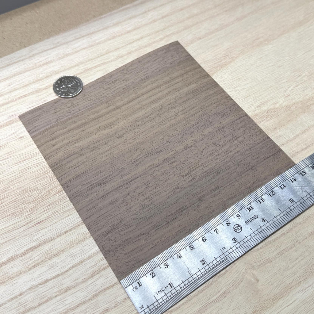 Walnut wood veneer sheet shown next to a ruler for scale, 5-7/8 inch square and 0.15 mm thick