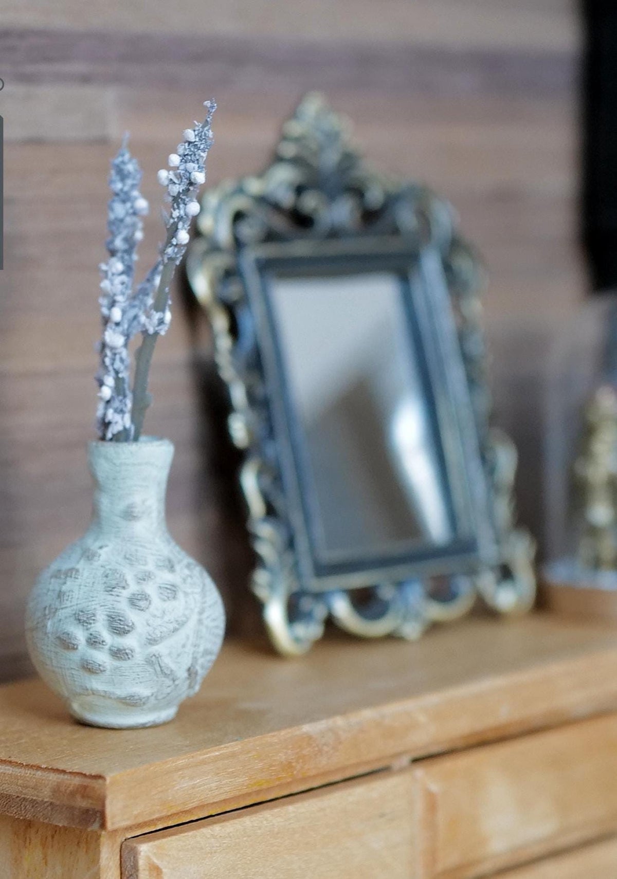 1:12 scale miniature whitewashed round clay vase with raised pebble pattern and silvery white flower stems, next to an ornate framed mirror on a wood dresser