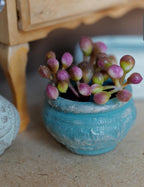 1:12 scale miniature weathered turquoise round clay pot with a rolled rim, planted with a cluster of pink and green flower buds
