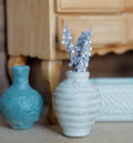 1:12 scale miniature whitewashed ribbed clay vase with silvery white flower stems, beside a teal vase under a wood side table
