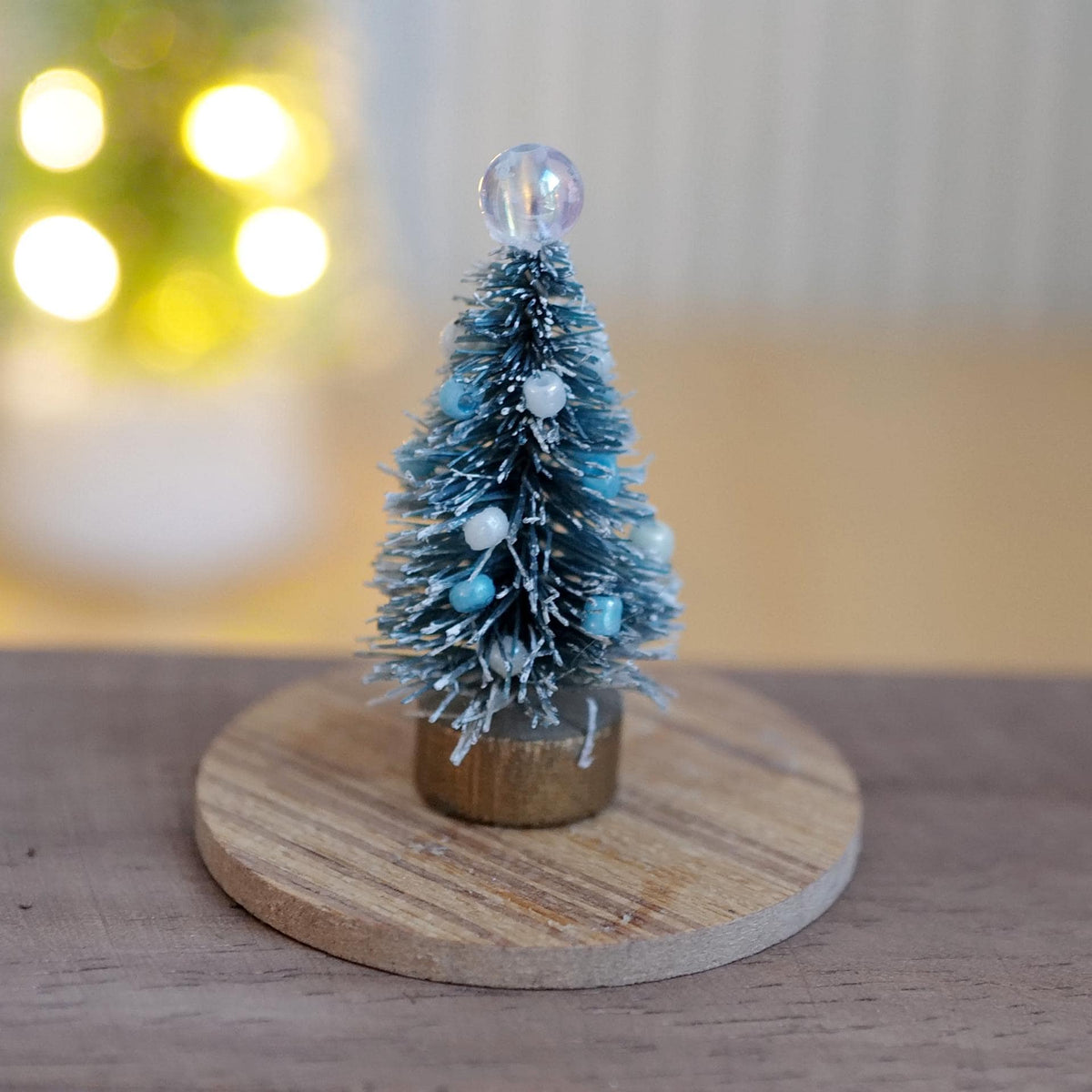 1:12 scale miniature frosted bottle brush Christmas tree with blue and white beads and a clear bead topper, shown on a round wood base