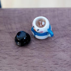 1:12 scale miniature white snowman mug with a blue scarf, filled with hot chocolate and marshmallows, with its black top hat lid beside it on a wood table
