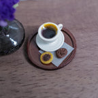 1:12 scale miniature cream cup of black coffee with crema on a saucer, with two chocolate cookies on deli paper, on a round brown serving tray