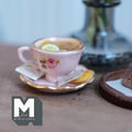 1:12 scale miniature pink cup and saucer with gold rims and a pink rose, filled with lemon tea and lemon slices, with a tea bag and a jam cookie on the saucer