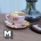 1:12 scale miniature pink cup and saucer with gold rims and a pink rose, filled with lemon tea and lemon slices, with a tea bag and a jam cookie on the saucer