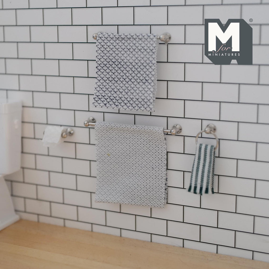 1:12 scale miniature silver towel bars, towel ring and toilet paper holder on a white subway tile wall, hung with gray patterned towels, a green and white striped hand towel and a paper roll