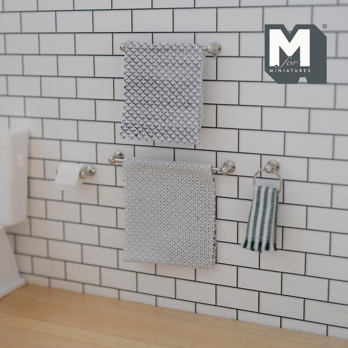 1:12 scale miniature silver towel bars, towel ring and toilet paper holder on a white subway tile wall, hung with gray patterned towels, a green and white striped hand towel and a paper roll