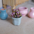 1:12 scale miniature clay potted plant, a weathered light green six-sided pot holding pink and green flower buds, on a wood floor