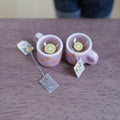 Two 1:12 scale miniature pink mugs with orange polka dots, filled with tea and lemon slices, with tea bags beside them on a wood table