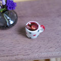 1:12 scale miniature white polka dot mug with red handle, filled with mulled wine, cinnamon stick and orange slice