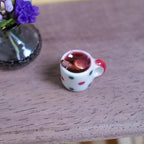 1:12 scale miniature white polka dot mug with red handle, filled with mulled wine, cinnamon stick and orange slice