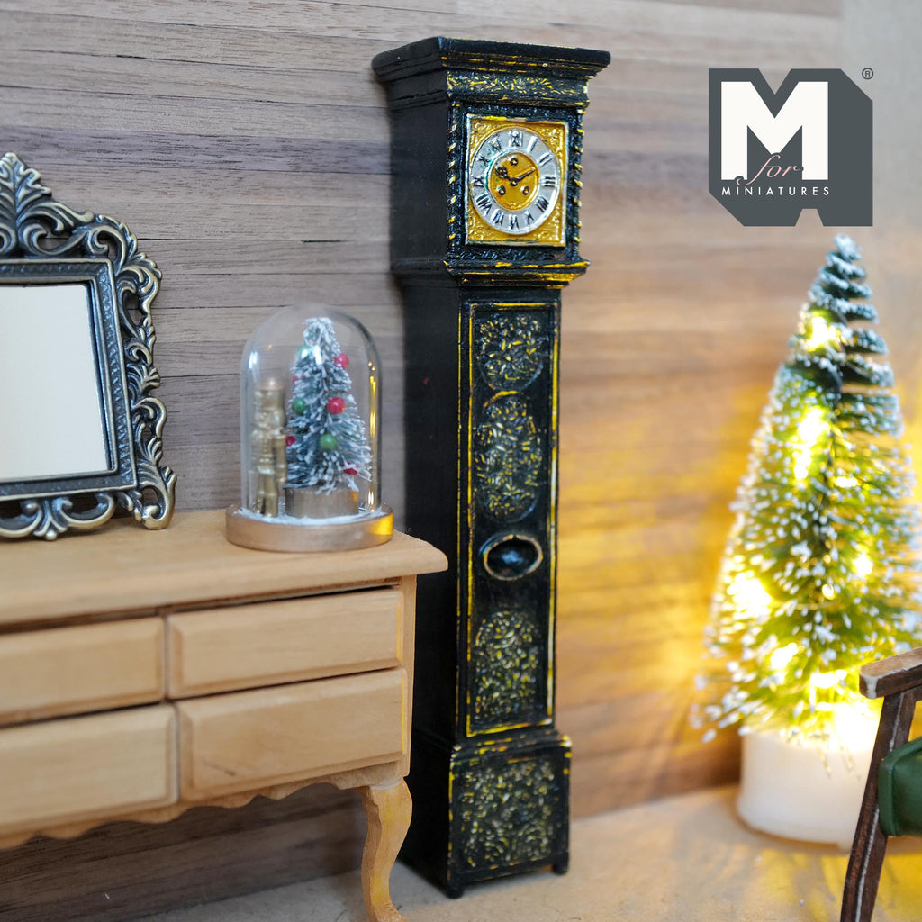 1:12 scale miniature weathered black grandfather clock with gold rim and decorated case, standing beside a dresser and a lit Christmas tree