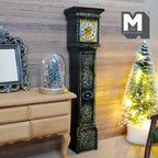 1:12 scale miniature weathered black grandfather clock with gold rim and decorated case, standing beside a dresser and a lit Christmas tree