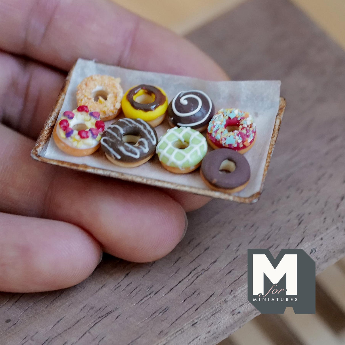 1:12 scale miniature tray of eight iced ring donuts in chocolate, pink, white with sprinkles, yellow and green on parchment on an aged metal baking tray