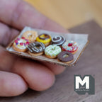 Donuts glacés miniatures sur plaque de cuisson en métal vieilli avec papier sulfurisé à l'échelle 1:12, lot de 9, 1-5/8 pouce de long, décoration pour maison de poupée