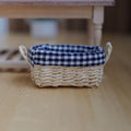 1:12 scale miniature oval woven basket with a navy and white gingham lining folded over the rim and loop handles on both ends, on a wood floor
