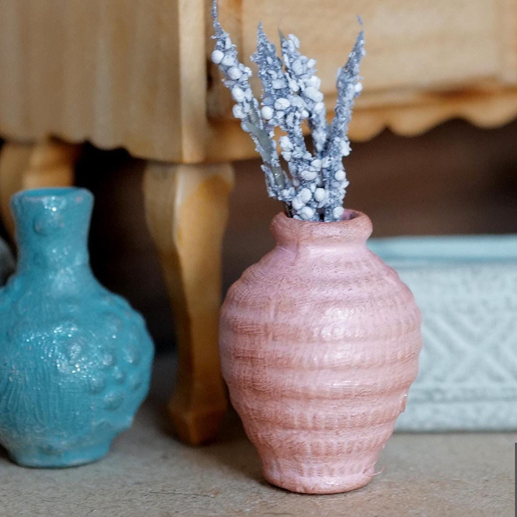 1:12 scale miniature pink ribbed clay vase with silvery white flower stems, beside a teal vase under a wood side table