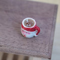 1:12 scale miniature ceramic Santa Claus face mug with a red handle, filled with hot chocolate and marshmallows, on a wood table