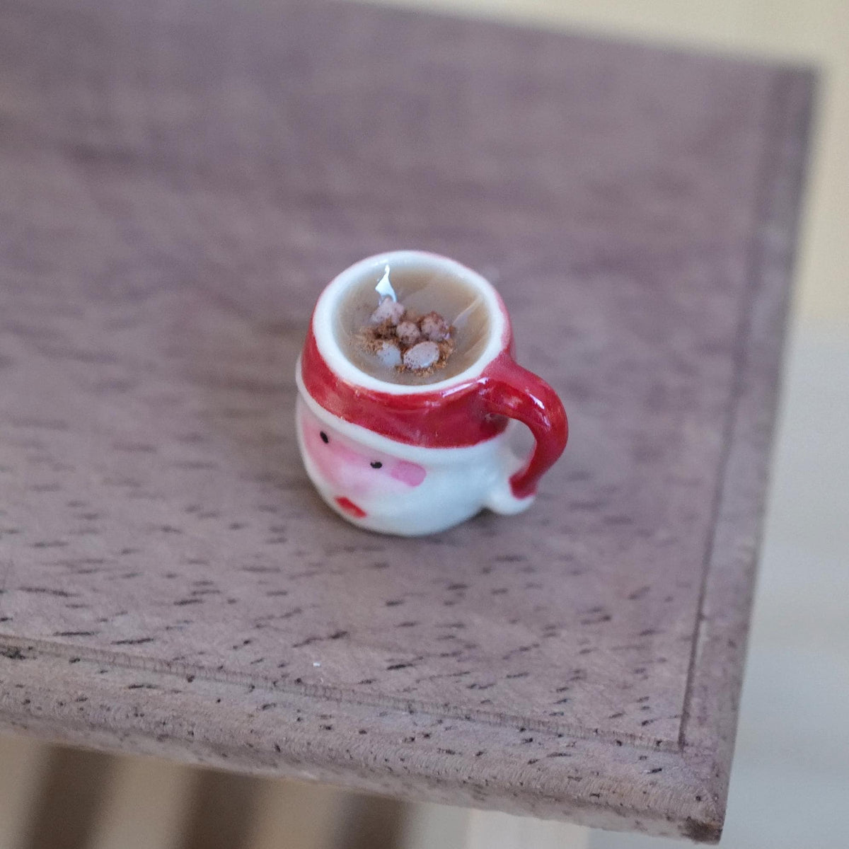 1:12 scale miniature ceramic Santa Claus face mug with a red handle, filled with hot chocolate and marshmallows, on a wood table