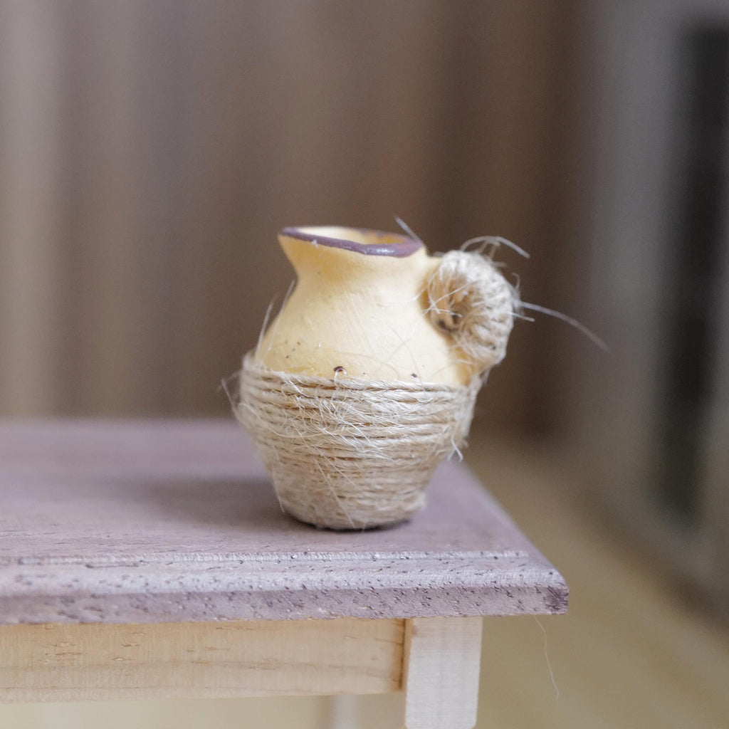1:12 scale miniature beige clay pitcher with a brown rim, wrapped in jute twine, on a wood table