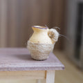 1:12 scale miniature beige clay pitcher with a brown rim, wrapped in jute twine, on a wood table