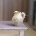1:12 scale miniature beige clay pitcher with a brown rim, wrapped in jute twine, on a wood table