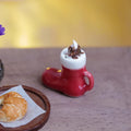 1:12 scale miniature red Santa boot mug with white cuff, topped with whipped cream and chocolate fudge, beside a croissant