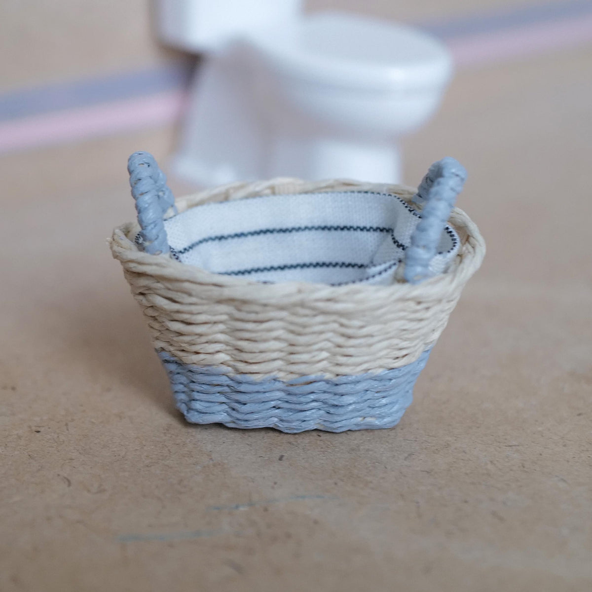 1:12 scale miniature two-tone woven laundry basket with a natural top, gray lower band and gray handles, lined with white and navy striped fabric